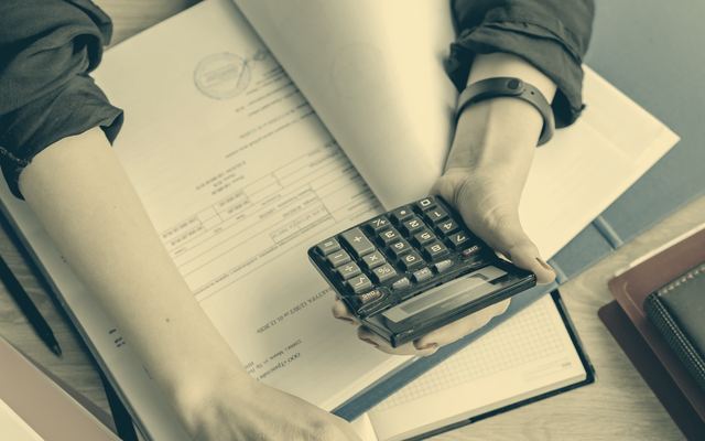 Dłonie nad dokumentami, kalkulatorem i laptopem na biurku