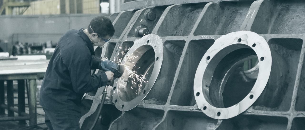 Pracownik szlifujący kołnierz dużego odlewu, snop iskier w hali produkcyjnej