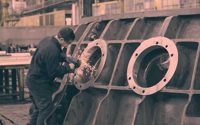 Pracownik szlifujący kołnierz dużego odlewu, snop iskier w hali produkcyjnej